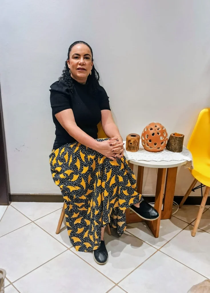 Dra. Denise Lopes sentada, em retrato com roupa preta e detalhes amarelos